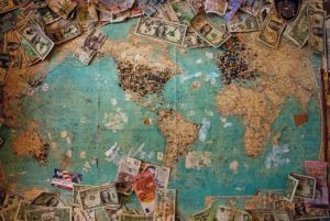 Overhead view of a world map with many us dollar bills strewn across the top and bottom edges
